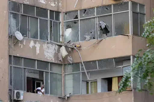 A Lebanese man looks through his apartment window at the scene where an Israeli airstrike hit a building early Monday, Sept. 30, 2024. (AP Photo/Hussein Malla)