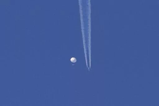 In this photo provided by Brian Branch, a large balloon drifts above the Kingstown, N.C. area, with an airplane and its contrail seen below it. The United States says it is a Chinese spy balloon moving east over America at an altitude of about 60,000 feet (18,600 meters), but China insists the balloon is just an errant civilian airshipused mainly for meteorological research that went off course due to winds and has only limited “self-steering” capabilities. (Brian Branch via AP)