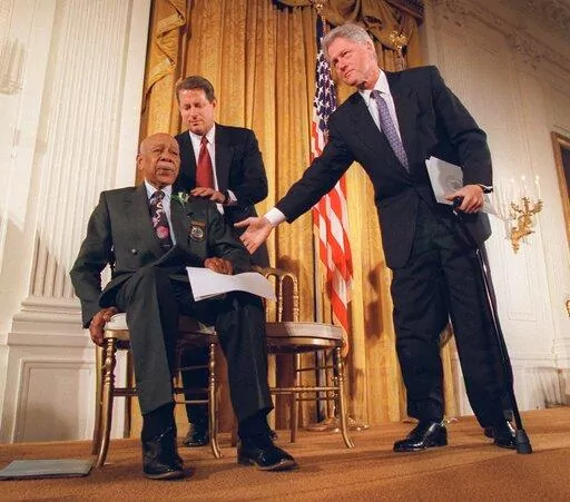 President Clinton and Vice President Al Gore, back, help Herman Shaw, 94, a Tuskegee Syphilis Study victim, during a news conference on May 16, 1997. Fifty years after the infamous Tuskegee syphilis study was revealed to the public in 1972 and halted, Manhattan-based philanthropy organization Milbank Memorial Fund is publicly apologizing for its role in the infamous Tuskegee syphilis study. (AP Photo/Doug Mills, File)