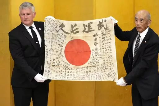 USS Lexington Museum executive director Steve Banta, left, and Toshihiro Mutsuda, the elderly son of Japanese soldier Shigeyoshi Mutsuda, hold together Mutsuda's good luck flag during the handover ceremony of his good luck flag at Yasukuni shrine in Tokyo, Japan, Saturday, July 29, 2023. Mutsuda was only 5 years old when he last saw his father, who was drafted by Japan's Imperial Army in 1943 and killed in action. For him, his father was a bespectacled man in an old family photo standing by a si