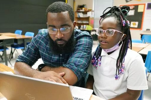 Ryan Johnson, a fifth-grade teacher at Pecan Park Elementary School, left, checks to see what homework his daughter, Rylei, is bringing home, as they prepare to leave Johnson's classroom in Jackson, Miss., Tuesday, Sept. 6, 2022. Because the city's long-standing water issues recently forced the public schools to again revert to remote learning, Johnson brought his daughter to work where she could be monitored as she also attended virtual classes, while he taught his students virtually. (AP Photo