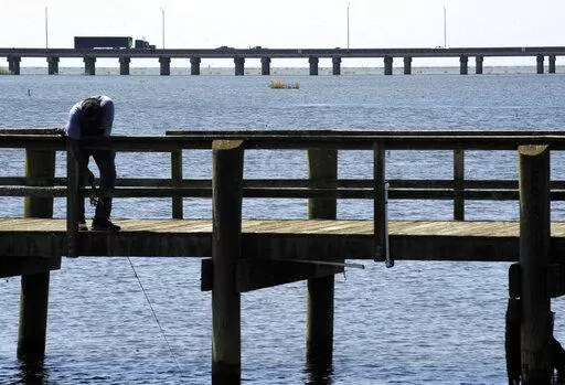 A man fishes on a pier as traffic on Interstate 10 crosses Mobile Bay at Spanish Fort, Ala., on Wednesday, Aug. 28, 2019. A $2.7 billion plan to ease traffic along the northern Gulf Coast in Alabama with the construction of a new Interstate 10 bridge and highway through Mobile has taken a step forward. (AP Photo/Jay Reeves)