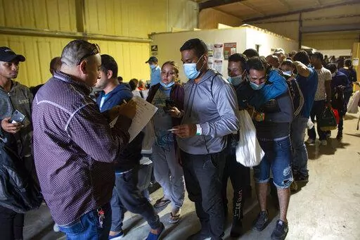 People line up for a commercial bus that will take them to the San Antonio airport at a warehouse run by the Mission: Border Hope nonprofit group run by the United Methodist Church in Eagle Pass, Texas, May 23, 2022. U.S. immigration authorities are planning to issue photo ID cards to immigrants in deportation proceedings in a bid to slash paper use and help people stay up-to-date on required meetings and court hearings, officials said. (AP Photo/Dario Lopez-Mills, File)