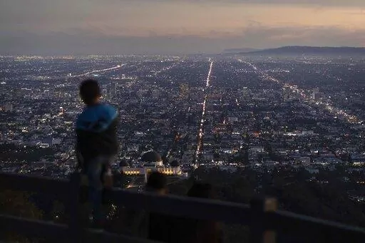 A boy takes in the view of the Los Angeles skyline from the Griffith Park Observatory Trails Peak in Los Angeles, Monday, Nov. 14, 2022. The 8 billionth baby on Earth is about to be born on a planet that is getting hotter. But experts in climate science and population both say the two issues aren't quite as connected as they seem. (AP Photo/Jae C. Hong)