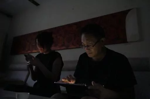 Wang Quanzhang and his wife Li Wenzu look at their phone and laptop in the dark after power was cut off for their apartment in Beijing's Changping district, Tuesday, June 20, 2023. Disbarred human rights lawyer Wang Quanzhang has been forced to move 13 times in two months as part of a pattern of harassment against him and three other prominent rights advocates in Beijing that is further squeezing the country's battered civil rights community. (AP Photo/Ng Han Guan)