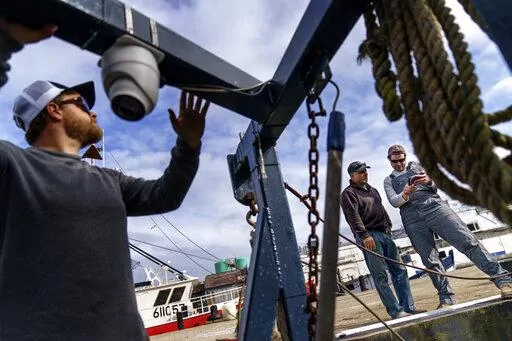 Mark Hager, left, positions a camera with the help of Anthony Lucia, right, as captain Al Cottone watches the feed on a monitor from his boat, the Sabrina Maria, in Gloucester, Mass., May 11, 2022. Hager's Maine-based startup, New England Maritime Monitoring, is one of a bevy of companies seeking to help commercial vessels comply with new federal mandates aimed at protecting dwindling fish stocks. But taking the technology overseas, where the vast majority of seafood consumed in the U.S. is caug