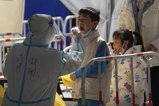 A health worker in protective suit takes a throat swab sample from a child at a coronavirus testing site, Monday, March 21, 2022, in Beijing, China. Disney Co. closed its Shanghai theme park Monday as Chinese authorities tried to control the city's biggest coronavirus flareup in two years, while the southern business center of Shenzhen allowed shops and offices to reopen after a weeklong closure. (AP Photo/Andy Wong)