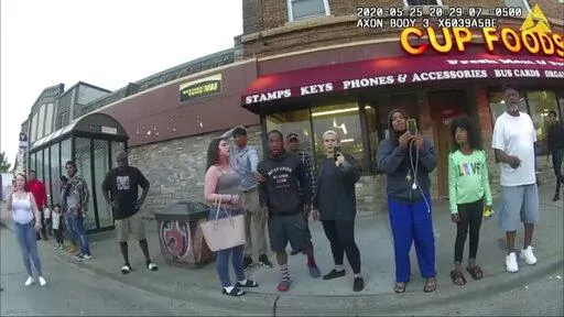 In this image from a police body camera, bystanders, including Alyssa Funari, filming at left; Charles McMillan, center left in light colored shorts; Christopher Martin, center in gray, with hand on head; Donald Williams, center in shorts; Genevieve Hansen, filming, fourth from right; Darnella Frazier, filming, third from right, witness as then Minneapolis police officer Derek Chauvin pressed his knee on George Floyd's neck for several minutes, killing Floyd on May 25, 2020, in Minneapolis. Fraz