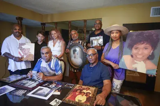 Descendants of Nelson Bell, brothers Milford Fonza, front left, and Elmer Fonza, front right, surrounded by extended family members, show their ancestors' pictures in Glendora, Calif., on Friday, Sept. 8, 2023. Family members standing from left: Trent Mure, with son Armani Mure, and his wife Tami Mure, William Woolery, Louie Hobbs and Carolyn Fonza. (AP Photo/Damian Dovarganes)
