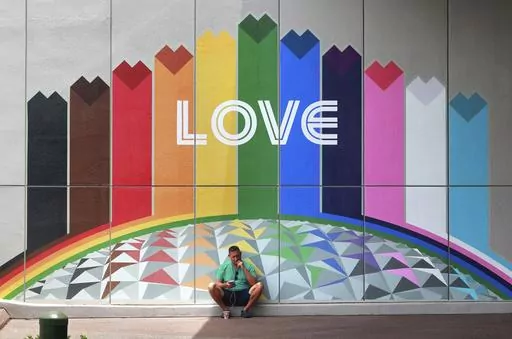 A guest finds a shady spot as a respite from the heat in front of a colorful mural adjacent to the Connections Cafe at Epcot at Walt Disney World, in Lake Buena Vista, Fla., Monday, July 10, 2023. The weather forecast calls for more of the same this week across Central Florida, with sticky humidity, highs in the low 90s and a chance of afternoon and evening thunderstorms. (Joe Burbank/Orlando Sentinel via AP)