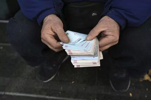 A street money exchanger poses for a photo without showing his face as he counts Iranian banknotes at a commercial district in downtown Tehran, Iran, Friday, Dec. 23, 2022. Iran’s currency fell to a record low on Sunday, plunging to 613,500 to the dollar, as its people celebrated the Persian New Year. (AP Photo/Vahid Salemi, File)