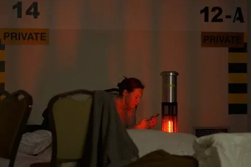 A woman looks at her mobile phone in a hotel underground parking turned into a bomb shelter during an air raid alert in Kyiv, Ukraine, Sunday, Feb. 27, 2022. Terrified men, women and children sought safety inside and underground, and the government maintained a 39-hour curfew to keep people off the streets as more than 150,000 Ukrainians fled to neighboring countries and the United Nations warned the number could grow to 4 million if fighting escalates.(AP Photo/Vadim Ghirda)