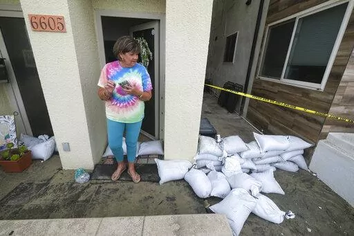 Sue Allen stands next to the sandbags lining at her home after a tropical storm on Saturday, Sept. 10, 2022, in Long Beach, Calif. Southern Californians welcomed cooler temperatures and spotty rain Saturday from a tropical storm veering off the Pacific Coast days after a relentless heat wave nearly overwhelmed the state's electrical grid. (AP Photo/Ringo H.W. Chiu)
