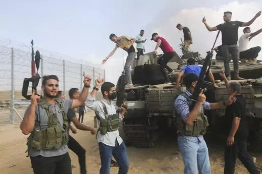Palestinian militants, some with guns raised in the air, celebrate by an Israeli tank at the border fence of the Gaza Strip on Oct. 7, 2023. The militant Hamas rulers of the Gaza Strip carried out an unprecedented, multi-front attack on Israel at daybreak, firing thousands of rockets as dozens of Hamas fighters infiltrated the heavily fortified border in several locations by air, land, and sea and catching the country off-guard on a major holiday. (AP Photo)