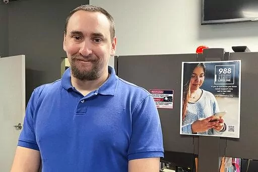 988 Call Center Director Jamieson Brill poses for a photo in front of a desk where work workers take calls around the clock at a facility in Hyattsville, Md., Oct. 7, 2022. Brill works in one of more than 200 call centers fanned out around the country tasked with answering an uptick in calls around the clock from people considering suicide or experiencing a mental health emergency. (AP Photo/Amanda Seitz)