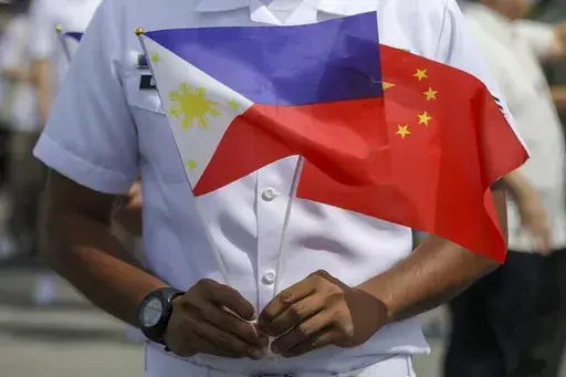 A member of the Philippine Coast Guard holds flags during the arrival of Chinese naval training ship, Qi Jiguang, for a goodwill visit at Manila's port, Philippines, June 14, 2023. (AP Photo/Basilio Sepe, File)