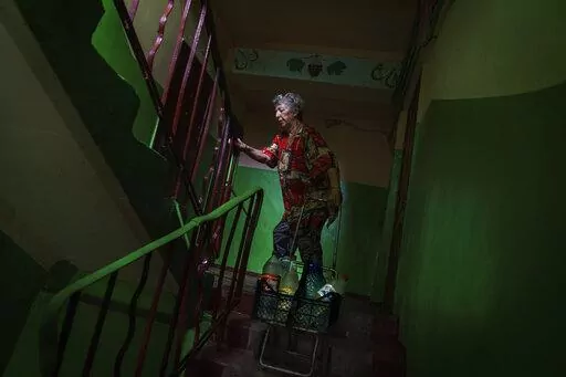 Lyubov Mahlii, 76, pulls a crate of water bottles up the stairs to her fifth floor apartment after filling them up at a nearby park in Sloviansk, Donetsk region, eastern Ukraine, Saturday, Aug. 6, 2022. A lack of running water in the city means that residents must fill bottles by hand at public pumps. While the remaining population has adapted to this new way of life, local officials warn that the coming of winter could set the stage for a humanitarian crisis. (AP Photo/David Goldman)