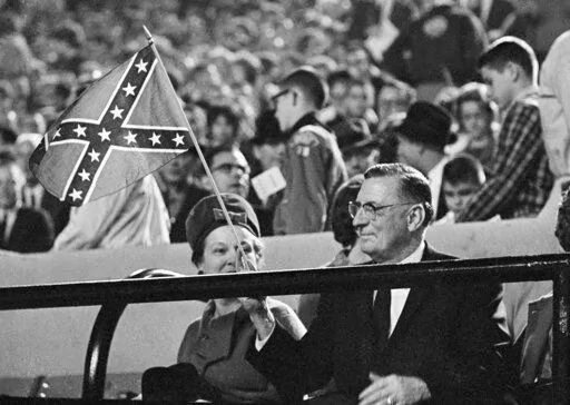 Mississippi Gov. Ross Barnett waves a confederate flag before the start of Ole Miss-Kentucky football game at the stadium on Sept. 29, 1962, in Jackson, Miss. With Barnett is his wife, the former Pearl Crawford, left. Mississippi in 2022 is on the verge of retiring a state song with racist roots, two years after it surrendered a Confederate-themed state flag. “Go, Mississippi" uses the tune of a 1959 campaign song for Ross Barnett, who won the governor's race proclaiming support of segregation