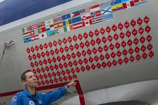 Lt. Commander Sam Urato, a P-3 pilot of National Oceanic and Atmospheric Administration, points to decals on the fuselage of the Lockheed WP-3D Orion 'hurricane hunter' aircraft representing the hurricanes it has penetrated during a hurricane awareness tour at Washington National Airport, Arlington, Va., Tuesday, May 3, 2022. Hurricane season starts Wednesday, June 1, 2022, and it's looking busy because every factor out there is pointing to another nasty year in the Atlantic. (AP Photo/Gemunu Am