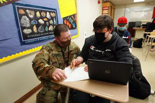 New Mexico Army National Guard specialist Michael Stockwell kneels while helping Alamogordo High School freshman Aiden Cruz with a geology assignment, at Alamogordo High School,Tuesday, Feb. 8, 2022, in Alamogordo, N.M. Dozens of National Guard Army and Air Force troops in New Mexico have been stepping in for an emergency unlike others they have responded to before: the shortage of teachers and school staff members that have tested the ability of schools nationwide to continue operating during t