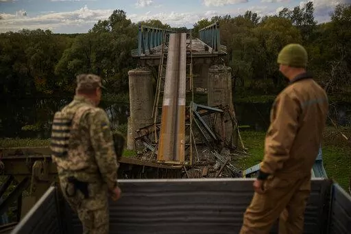 Ukrainian soldiers remove metal structure pieces as they work on a bridge damaged during fighting with Russian troops in Izium, Ukraine, Monday, Oct. 3, 2022. A series of embarrassing military losses for Moscow in recent weeks has presented a growing challenge for prominent hosts of Russian news and political talk shows scrambling to find ways to paint Kyiv's gains in a way that is still favorable to the Kremlin. (AP Photo/Francisco Seco)