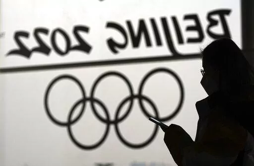 A woman looks at her phone as she passes an Olympic logo inside the main media center for the 2022 Winter Olympics, Jan. 18, 2022, in Beijing. (AP Photo/David J. Phillip, File)