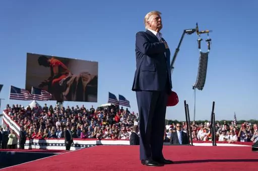 Former President Donald Trump stands while a song, "Justice for All," is played during a campaign rally at Waco Regional Airport, March 25, 2023, in Waco, Texas. The song features a choir of men imprisoned for their role in the Jan. 6, 2021, insurrection at the U.S. Capitol singing the national anthem and a recording of Trump reciting the Pledge of Allegiance. (AP Photo/Evan Vucci)