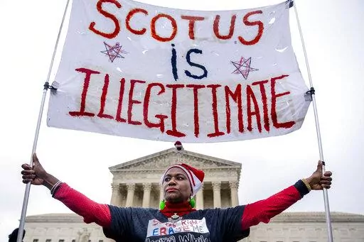 Nadine Seiler of Waldorf, Md., holds a sign that reads "SCOTUS is Illegitimate" in front of the Supreme Court in Washington, Wednesday, Dec. 7, 2022, as the Court hears arguments on a new elections case that could dramatically alter voting in 2024 and beyond. The case is from highly competitive North Carolina, where Republican efforts to draw congressional districts heavily in their favor were blocked by a Democratic majority on the state Supreme Court. (AP Photo/Andrew Harnik)