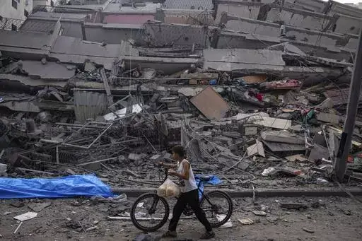 A Palestinian child walks with a bicycle by the rubble of a building after it was hit by an Israeli airstrike, in Gaza City, Sunday, Oct. 8, 2023. A new U.N. report paints a stark picture of the devastating collapsing Palestinian economy after a month of war and Israel’s near total siege of Gaza. (AP Photo/Fatima Shbair, File)