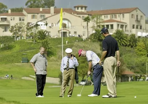 With the historic clubhouse in the background, Duffy Waldorf takes a practice putt at the 10th green as veteran teaching pro Eddie Merrins, in the tie, and golfer Arron Oberholser, right, watch during a practice session for the Nissan Open at Riviera Country Club, Feb. 18, 2003, in Los Angeles. Merrins died Wednesday, Nov. 22, 2023, at age 91. (AP Photo/Reed Saxon, File)