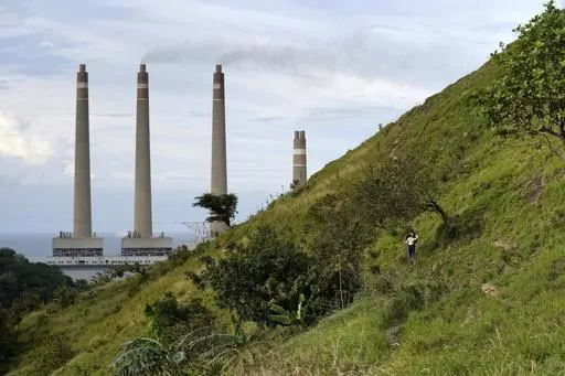 A couple walk on a hill called 'Teletubbies Hill', a locally popular tourist attraction, as the chimneys of Suralaya coal power plant looms in the background, in Cilegon, Indonesia, Sunday, Jan. 8, 2023. Asia must rapidly cut fossil fuel subsidies and plow more money into a clean energy transition to avoid catastrophic climate change that puts its own development at risk, according to a new report Thursday, April 27, from the Asian Development Bank. (AP Photo/Dita Alangkara)