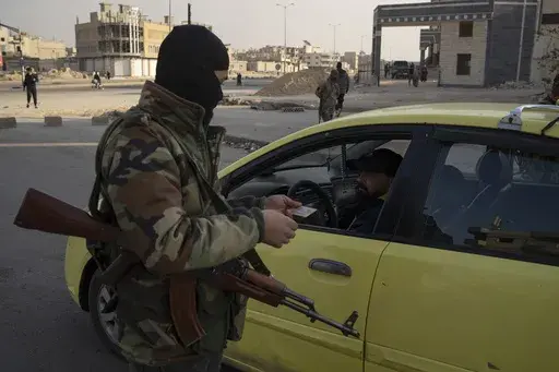 A member of the security forces of the newly formed Syrian government checks the ID of a driver at a security checkpoint in Homs, Syria, Thursday, Dec. 26, 2024. (AP Photo/Leo Correa)