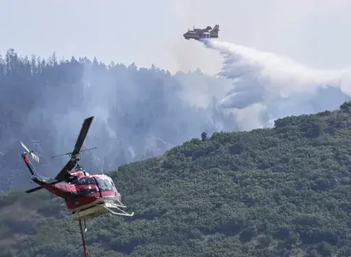 A CL 415 scooper, top, drops water on the Quarry Fire as a Firehawk helicopter maneuvers for a water drop Thursday, Aug. 1, 2024, southwest of Littleton, Colo. (Andy Cross/The Denver Post via AP)