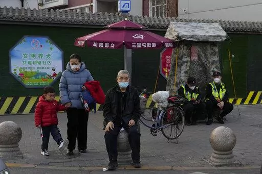 Residents wait to cross a road near members of the Chaoyang militia on duty in Beijing, Monday, March 6, 2023. Chinese economic officials expressed confidence Monday they can meet this year's growth target of "around 5%" by generating 12 million new jobs and encouraging consumer spending following the end of anti-virus controls that kept millions of people at home. (AP Photo/Ng Han Guan)