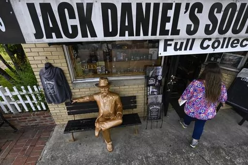 A statue of Jack Daniels sits on a bench as a visitor enters a souvenir shop in the town where the distillery is located Wednesday, June 14, 2023, in Lynchburg, Tenn. A destructive and unsightly black fungus which feeds on ethanol emitted by whiskey barrels has been found growing on property near the distillery's nearby barrelhouses which has resulted in a lawsuit against it. (AP Photo/John Amis)