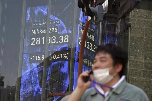A person wearing a protective mask walks in front of an electronic stock board showing Japan's Nikkei 225 index at a securities firm Tuesday, Aug. 9, 2022, in Tokyo. Asian shares mostly declined Tuesday amid a global fall in technology shares, including Japan's SoftBank, which has reported hefty losses caused by the market downturn. (AP Photo/Eugene Hoshiko)
