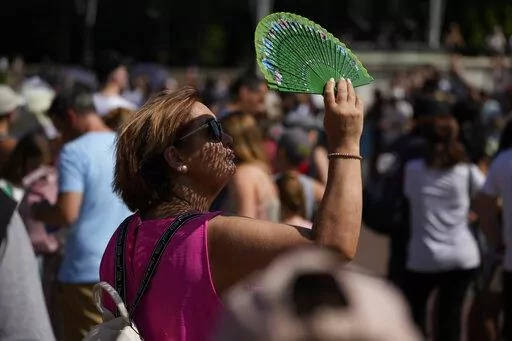 A tourist uses a fan to shade her face from the sun whilst waiting to watch the Changing of the Guard ceremony outside Buckingham Palace, during hot weather in London, July 18, 2022. Scientists said the heat wave in England and Wales on July 18 and 19 was definitely turbocharged by human-caused climate change, according to a study released Thursday, July 28, by the World Weather Attribution. (AP Photo/Matt Dunham, File)