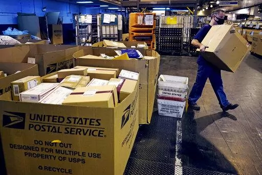 A worker carries a large parcel at the United States Postal Service sorting and processing facility Nov. 18, 2021, in Boston. Congress would lift onerous budget requirements that have helped push the Postal Service deeply into debt and would require it to continue delivering mail six days per week under bipartisan legislation that approached House approval Tuesday, Feb. 8, 2022. (AP Photo/Charles Krupa, File)