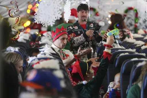 Flight attendant Gustavo Oliveira, center, juggles bubbles to entertain passengers during the United Airlines annual "fantasy flight" to a fictional North Pole at Denver International Airport, Saturday, Dec. 14, 2024, in Denver. (AP Photo/David Zalubowski)