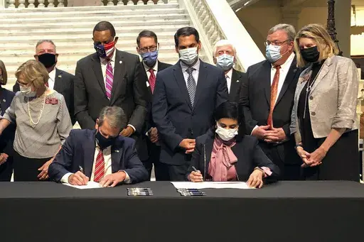 Georgia Gov. Brian Kemp, left, and Centers for Medicare and Medicaid Services Administrator Seema Verma, right, sign healthcare waivers at the state Capitol in Atlanta, Oct. 15, 2020. Pathways to Coverage launched last July and is the only Medicaid plan in the country that requires beneficiaries to work or engage in other activities to get coverage. As of June, it had about 4,300 members. (AP Photo/Jeff Amy, File)