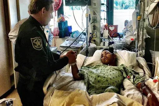 In this photo provided by the Broward County Sheriff's Office on Sunday, Feb. 18, 2018, Sheriff Scott Israel, holds the hand of Anthony Borges, 15, a student at Marjory Stoneman Douglas High School. Borges, the most severely wounded survivor of the 2018 massacre at Parkland's Marjory Stoneman Douglas High School, now owns shooter Nikolas Cruz's name and Cruz cannot give any interviews without his permission, under a settlement reached in a lawsuit, his attorney said Thursday, June 27, 2024. (Bro