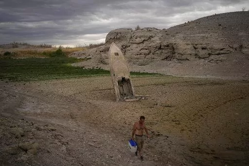A man walks by a formerly sunken boat standing upright into the air with its stern buried in the mud along the shoreline of Lake Mead amid a drought at the Lake Mead National Recreation Area near Boulder City, Nev., June 22, 2022. Costly weather disasters kept raining down on America last year, pounding the nation with 18 climate extremes that caused at least $1 billion in damage each, totaling more than $165 billion, federal climate scientists calculated Tuesday, Jan. 10, 2023. (AP Photo/John L