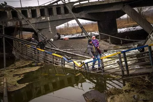 Local militiaman Valery, 37, carries a child as he helps a fleeing family across a bridge destroyed by artillery, on the outskirts of Kyiv, Ukraine, Wednesday, March 2. 2022.  Russian forces have escalated their attacks on crowded cities in what Ukraine's leader called a blatant campaign of terror. (AP Photo/Emilio Morenatti)