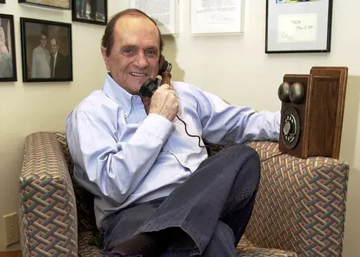 Comedian Bob Newhart pretends to speak on an antique telephone at his home in the Bel Air Estates community of Los Angeles, June 25, 2003. Newhart, the deadpan master of sitcoms and telephone monologues, died in Los Angeles on Thursday, July 18, 2024. He was 94. (AP Photo/Jerome T. Nakagawa, File)