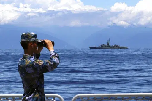 In this photo provided by China's Xinhua News Agency, a People's Liberation Army member looks through binoculars during military exercises as Taiwan's frigate Lan Yang is seen at the rear on Aug. 5, 2022. China on Wednesday, Aug. 10, reaffirmed its threat to use military force to bring self-governing Taiwan under its control, amid threatening Chinese military exercises that have raised tensions between the sides to their highest level in years. (Lin Jian/Xinhua via AP, File)