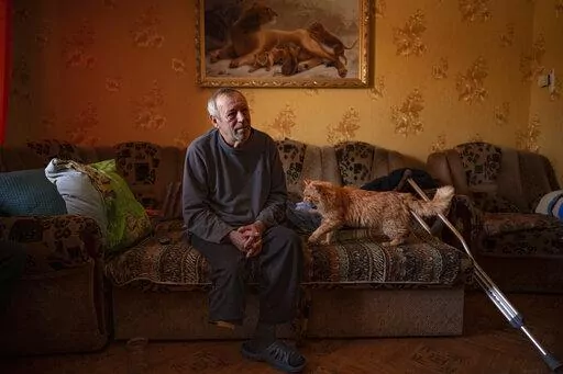 Land mine victim Oleksandr Rabenko, 66 years-old, speaks during an interview with the Associated Press as Murzik, his cat, approaches, at his son's home on the outskirts of Izium, Ukraine, Sunday, Feb. 19, 2023. In this war-scarred city in Ukraine's northeast, residents scrutinize every step for land mines. The brutality of the Russian invasion in this one-time strategic supply hub for Russian troops counts among the most horrific of the war, which entered its second year last month. (AP Photo/V
