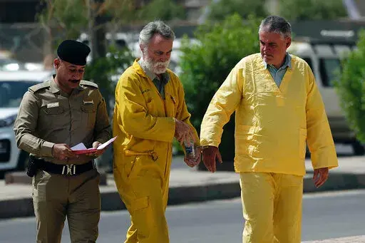 Volker Waldmann, right, and Jim Fitton, center, are handcuffed as they walk to a courtroom in Baghdad, Iraq, Sunday, May 22, 2022. Waldmann and Fitton, accused of smuggling ancient shards out of Iraq, appeared in a Baghdad court Sunday, telling judges they had not acted with criminal intent and had no idea they might have broken local laws. (AP Photo/Hadi Mizban)