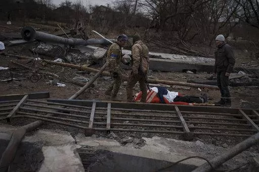 The body of a civilian, whose cause of death is unknown, lays on a stretcher on a path being used as an evacuation route out of Irpin, on the outskirts of Kyiv, Ukraine, Saturday, March 12, 2022. Kyiv northwest suburbs such as Irpin and Bucha have been enduring Russian shellfire and bombardments for over a week prompting residents to leave their homes. (AP Photo/Felipe Dana)