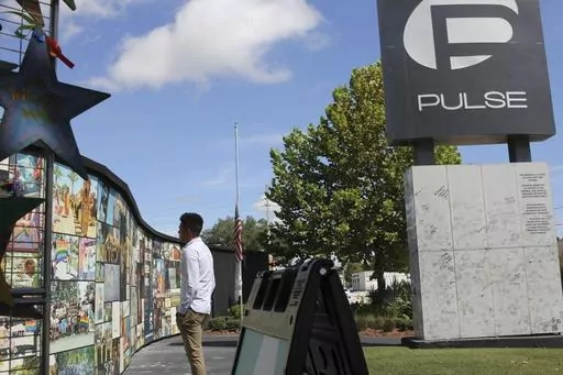 Brandon Wolf, a survivor of the Pulse nightclub shooting and activist, looks at the photos that are a part of the Pulse memorial in Orlando, Fla., on Sept. 9, 2022. The city of Orlando plans to purchase the gay nightclub property where 49 people were massacred seven years ago, in what at the time was the deadliest mass shooting in modern U.S. history, with the intention of building a memorial for the victims, Mayor Buddy Dyer said Wednesday, Oct. 18, 2023. (AP Photo/Cody Jackson, file)
