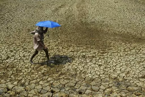 A villager holding umbrella to protect himself from sun, walks over parched land on the outskirts of Bhubaneswar, India on May 2, 2009. Tense negotiations at the final meeting on a climate-related loss and damages fund — an international fund to help poor countries hit hard by a warming planet — ended Saturday, Nov. 4, 2023, in Abu Dhabi, with participants agreeing that the World Bank would temporarily host the fund for the next four years.(AP Photo/Biswaranjan Rout, File)